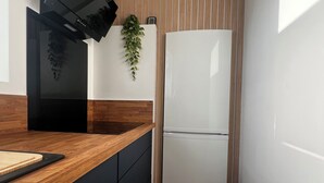Une cuisine avec une hotte noire, un réfrigérateur blanc, des armoires en bois, un plan de travail en bois et une plante suspendue.