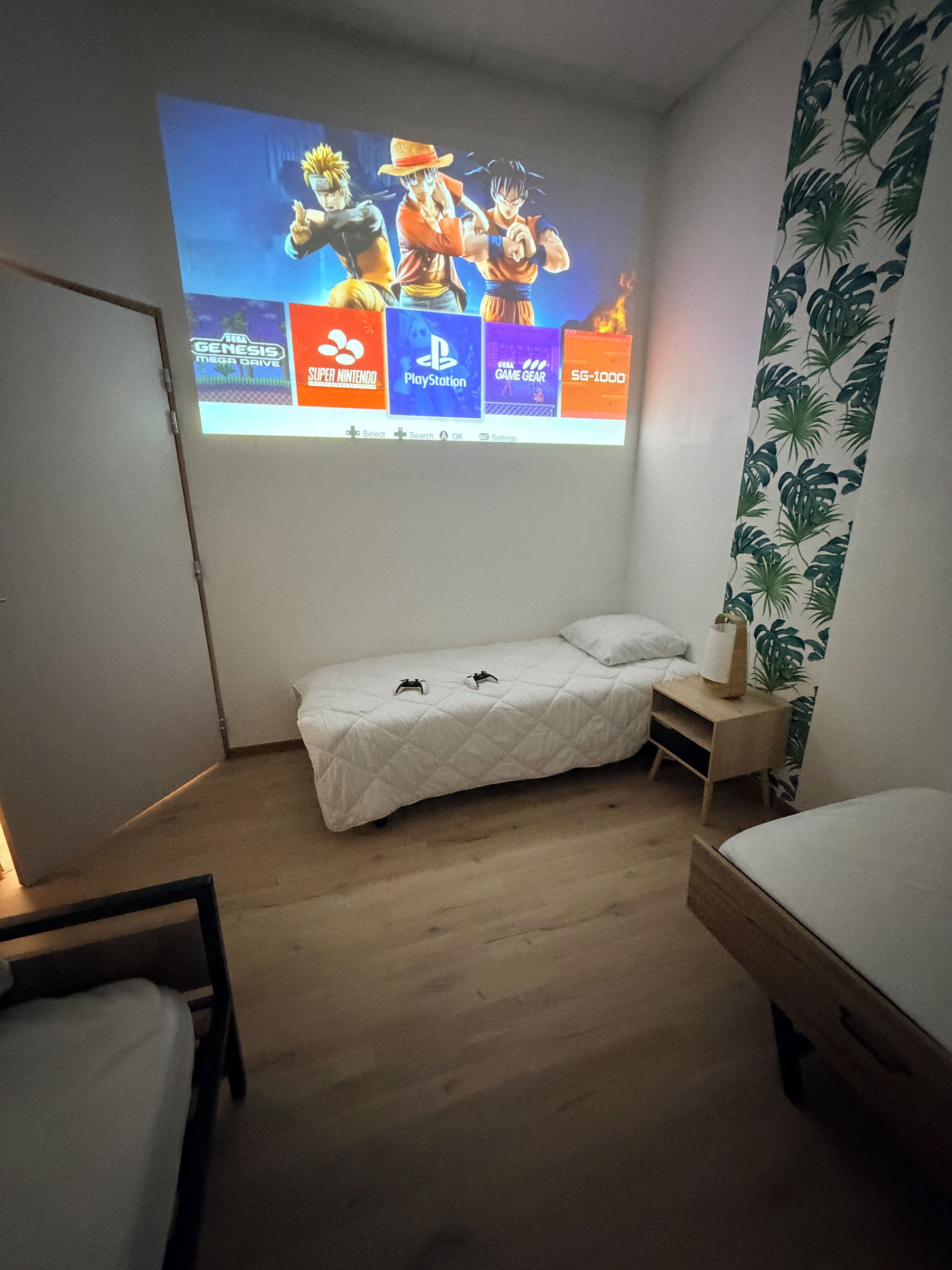Ett sovrum med en säng, ett sängbord och en väggmonterad projektor som visar ett datorspel.