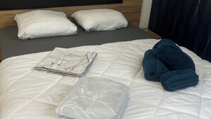 Un lit bien fait, avec une couette blanche, deux oreillers blancs, une couverture pliée et une paire de serviettes bleues.