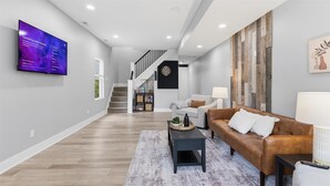 A modern living room with a flat-screen TV, a staircase, a brown leather sofa, and a coffee table. - Freshly renovated 2 story house near downtown Indy (Indianapolis)