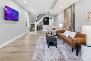 Ein modernes Wohnzimmer mit Flachbildfernseher, einer Treppe, einem braunen Ledersofa und einem Couchtisch.