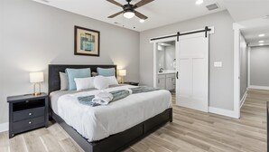 A bedroom with a bed, nightstands, a ceiling fan, a framed picture, a sliding door, and a bathroom visible through the door. - Freshly renovated 2 story house near downtown Indy (Indianapolis)