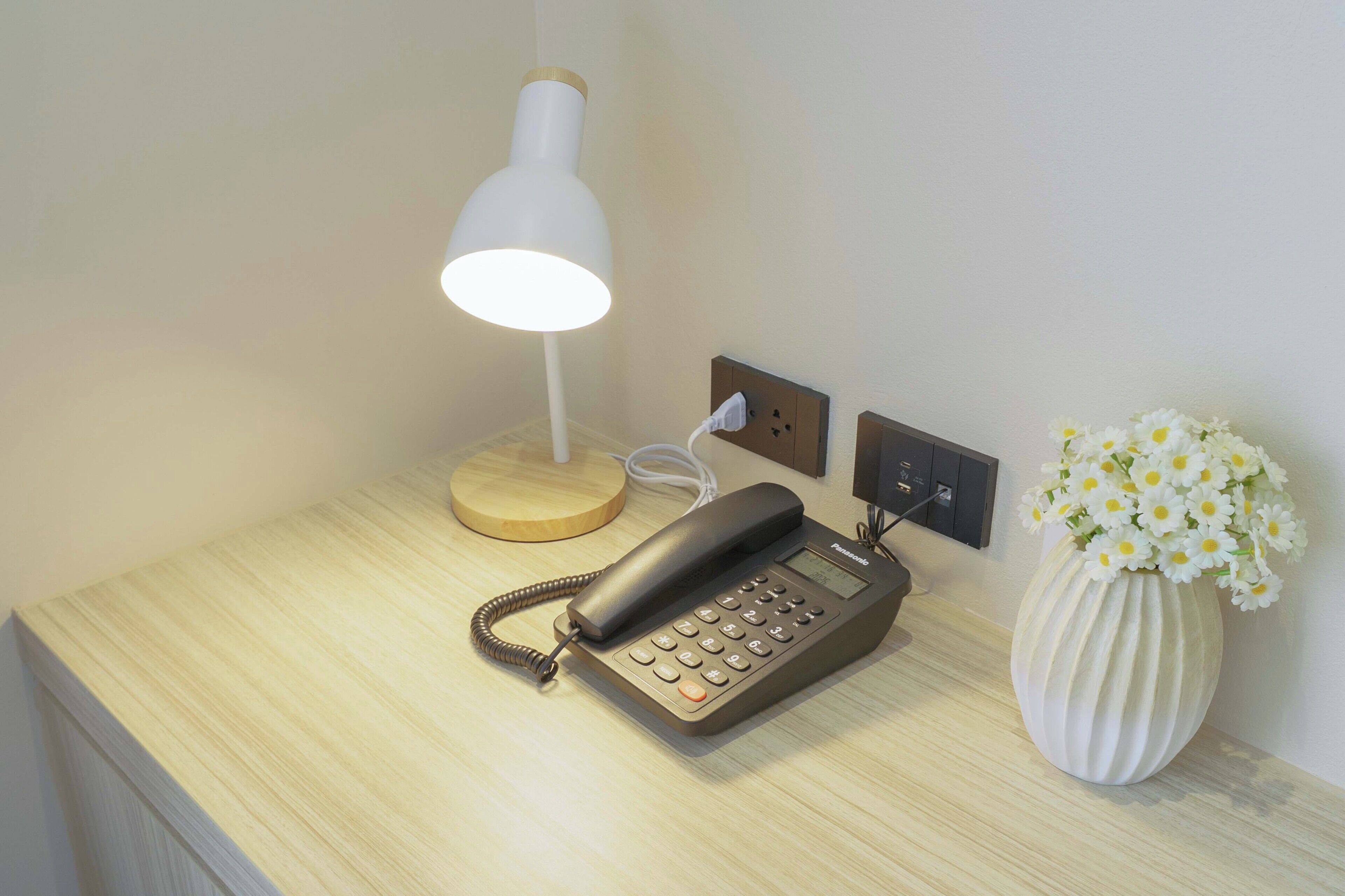 Ein Nachttisch mit Lampe, Telefon und Blumen in einer Vase.