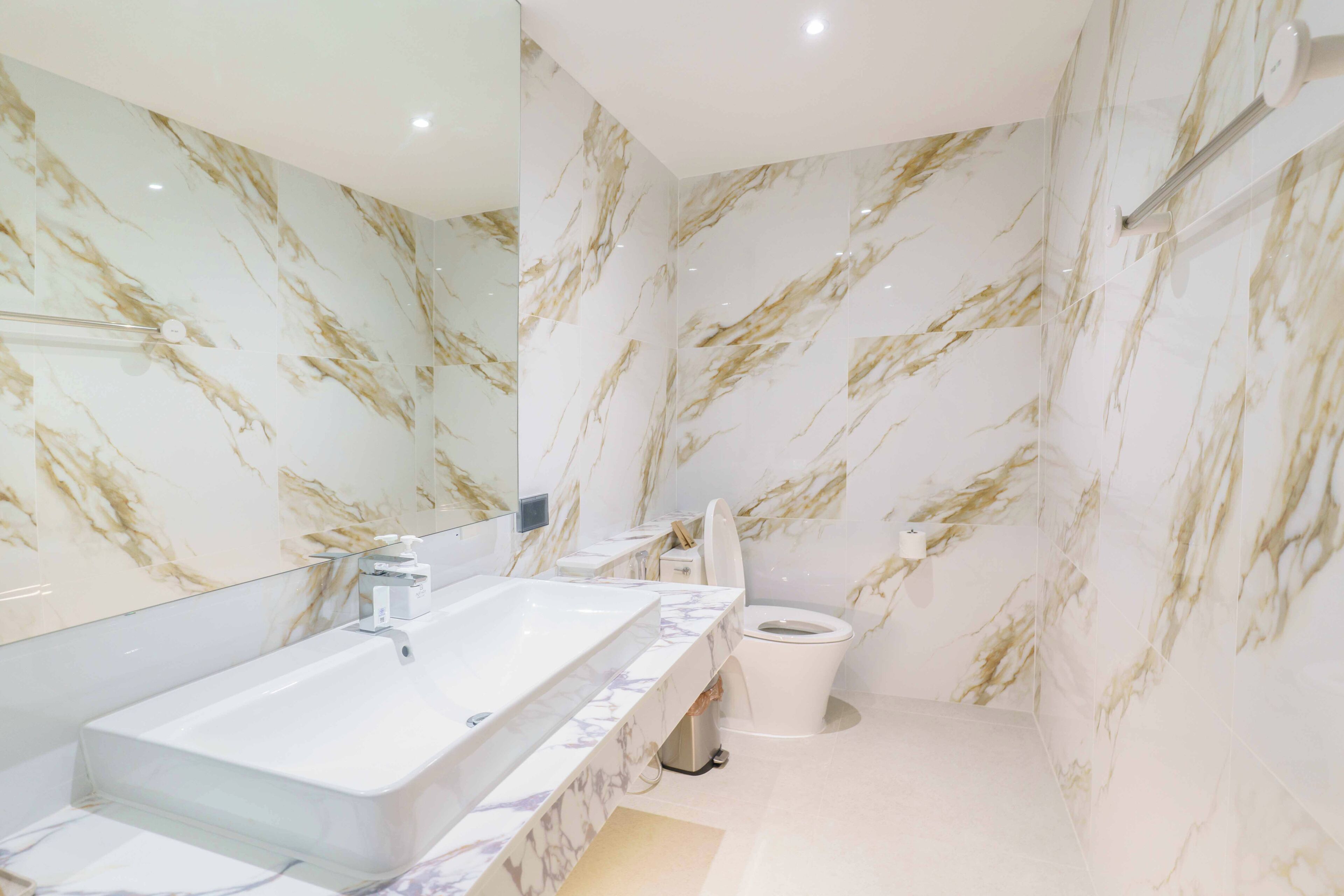 Un baño con pared de mármol, un lavabo blanco y un inodoro.