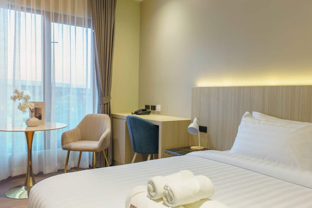Una habitación de hotel con cama, escritorio, silla, mesita y ventana con cortinas.