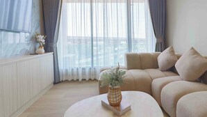 A modern living room with a sofa, a coffee table with a vase, and a TV mounted on the wall. - Sakhonburi Cozy Hotel (Samut Sakhon)