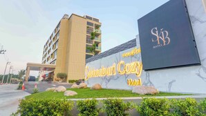 A hotel entrance with a large sign for 'Sakhonburi Cozy Hotel,' a modern building with a flat roof, and a clear sky. - Sakhonburi Cozy Hotel (Samut Sakhon)