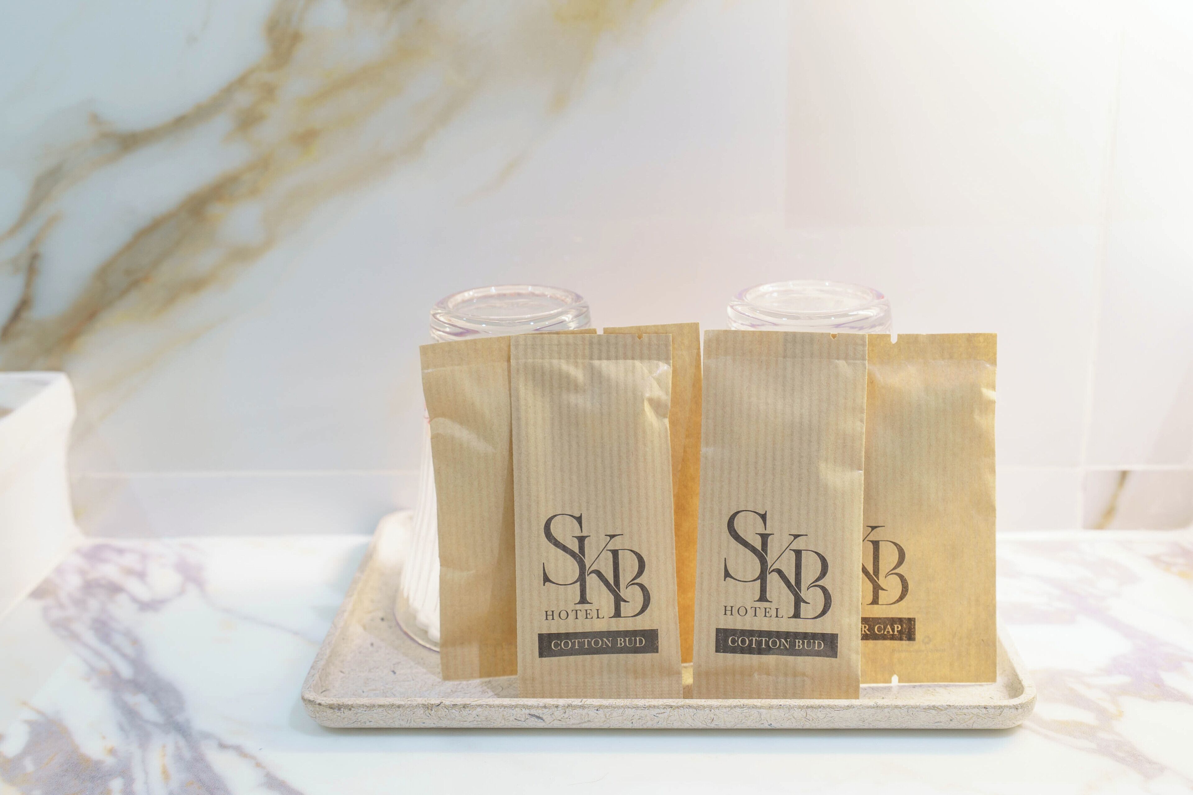 Trois sachets étiquetés « SkB Hotel Cotton Bud » sont posés sur une surface en marbre.