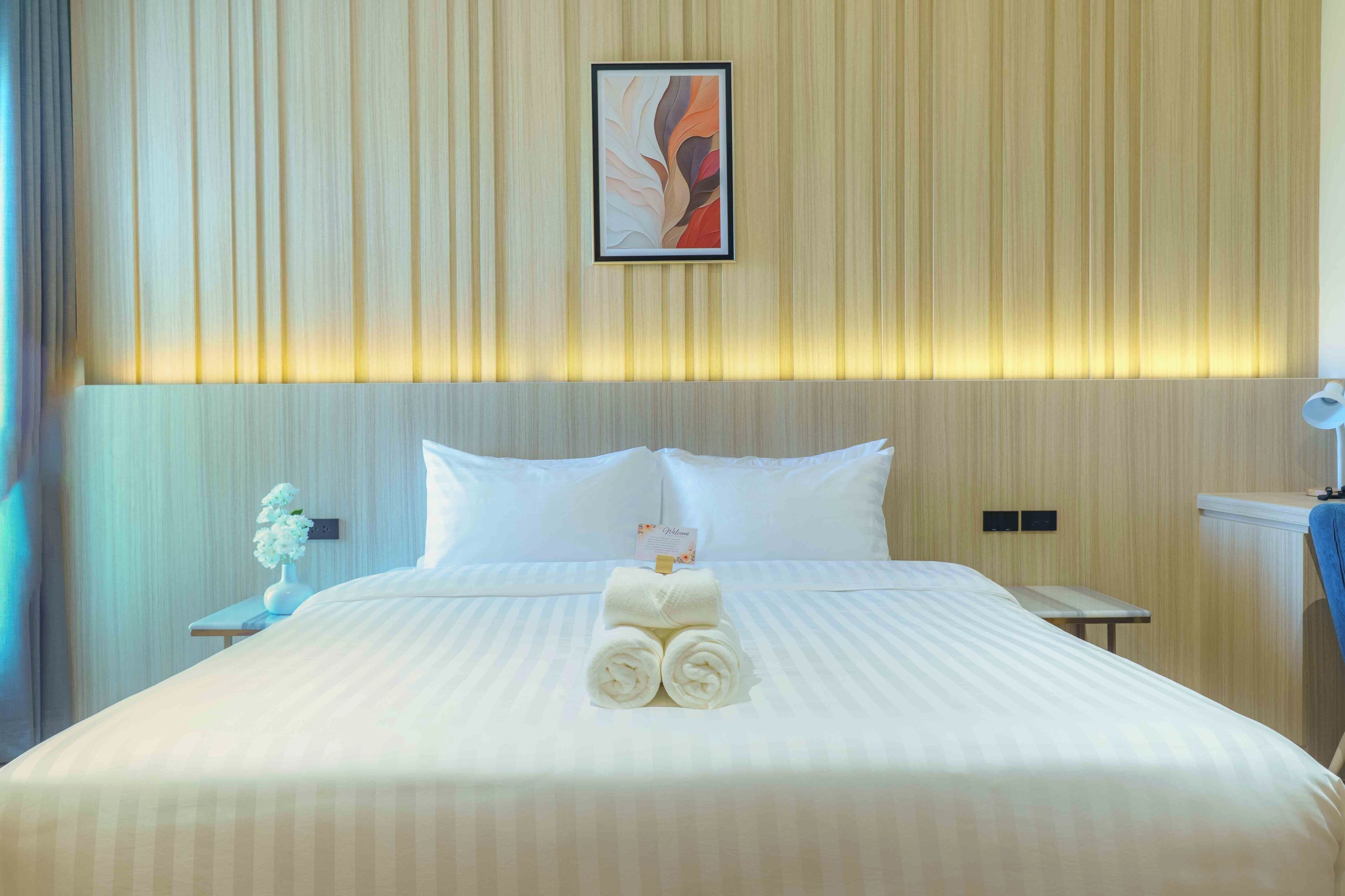 A hotel room with a large bed, a nightstand with a vase of flowers, a framed picture on the wall, and a blue chair.