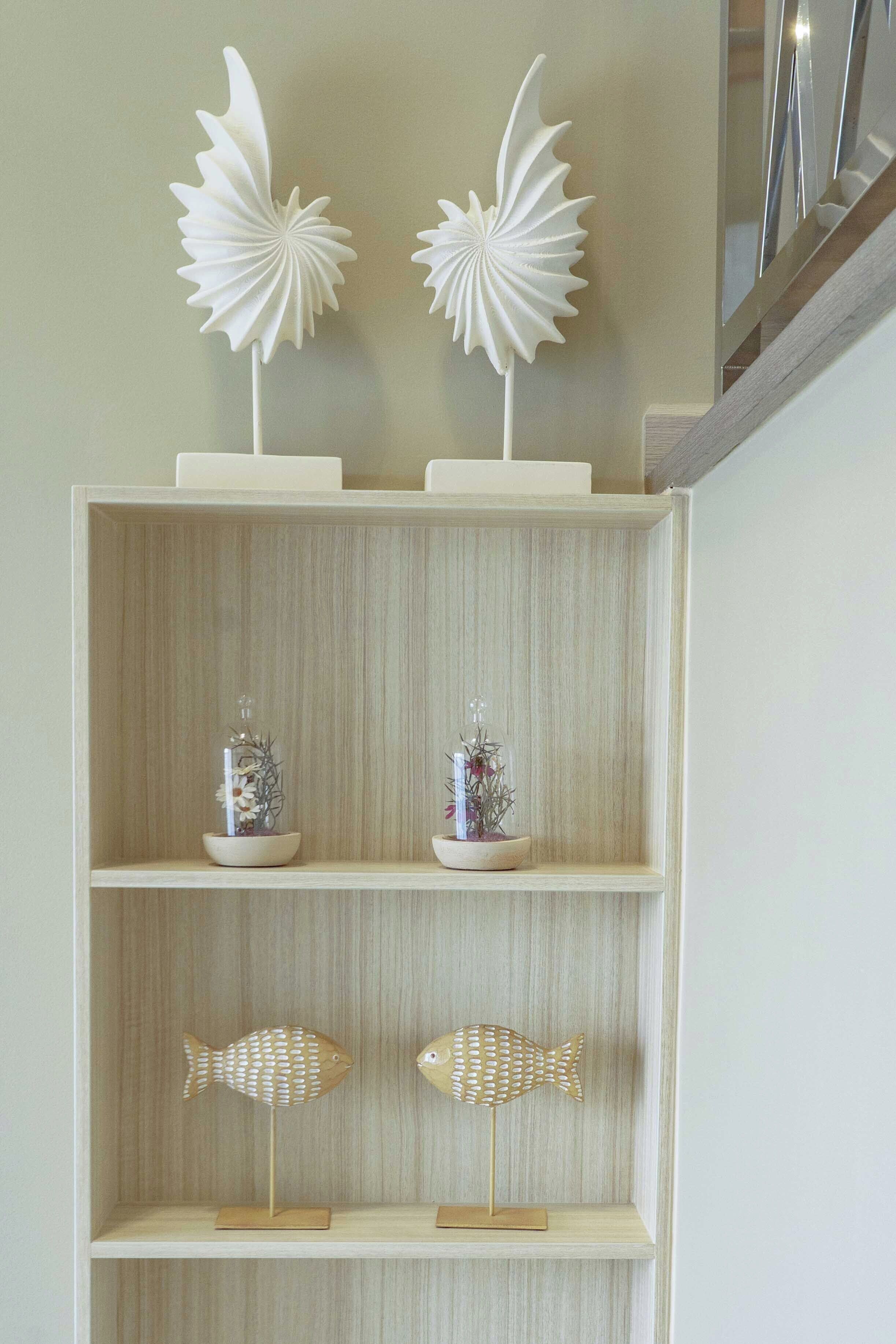 Estante de madera con adornos, incluyendo dos figuras que parecen pájaros blancos, dos jarrones de vidrio con flores y dos figuras de peces de madera.