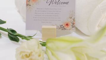 A welcome card on a bed with a floral design, a white rose, and a green lily.