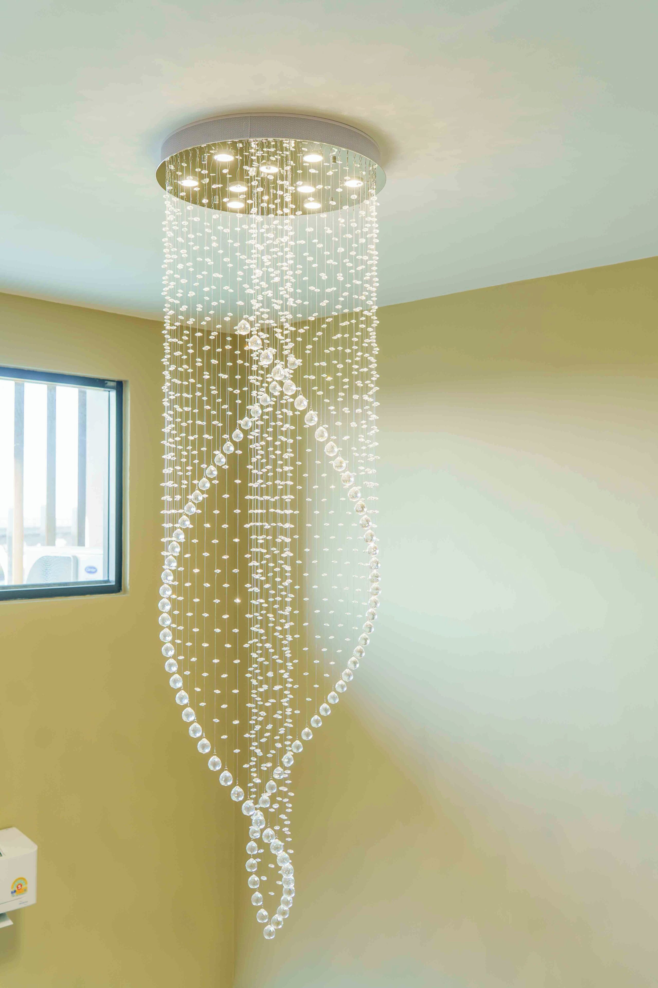 Un lustre composé de plusieurs lampes suspendues, dans une pièce dotée d’une fenêtre et d’un interrupteur fixé au mur.