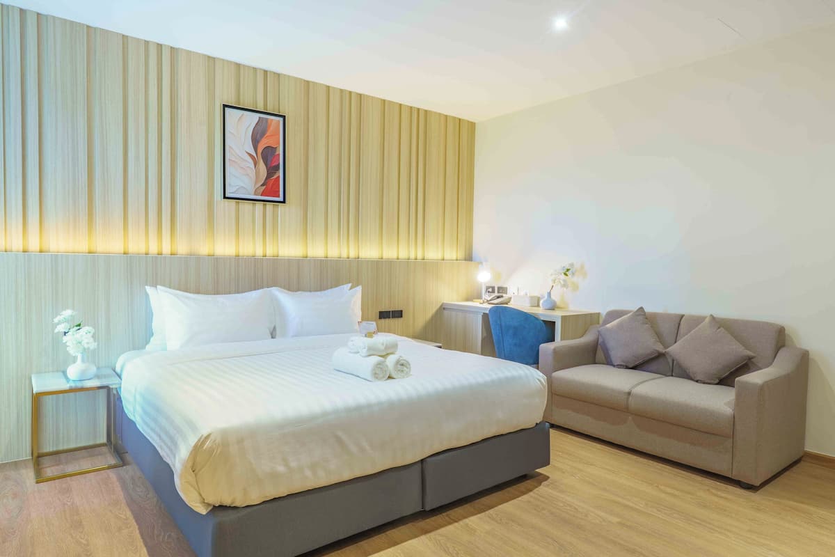 Habitación de hotel con cama, sofá, mesita de noche con lámpara y una obra de arte colgada en la pared.