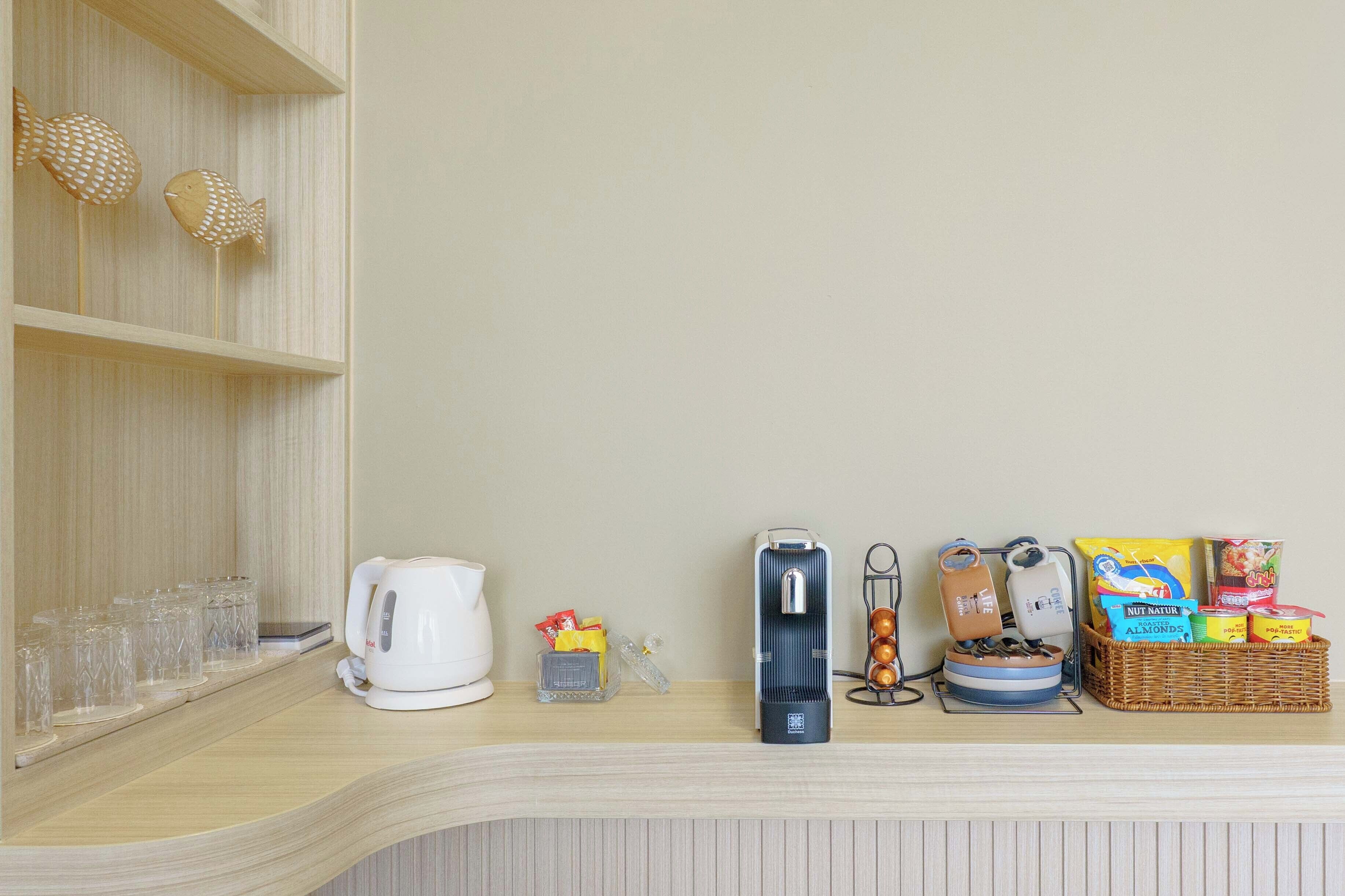 A kitchen counter with a kettle, a coffee maker, a rice cooker, a fruit basket, and a glass set.