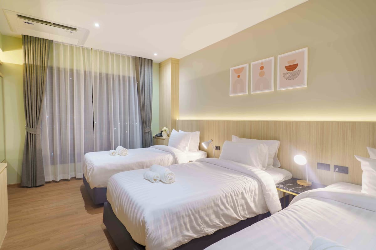 Habitación de hotel con dos camas, una mesita de noche con lámpara, aire acondicionado de pared y un amplio ventanal con cortinas.
