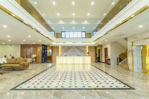 A spacious lobby with a marble floor, a reception desk, and a staircase leading to upper floors.