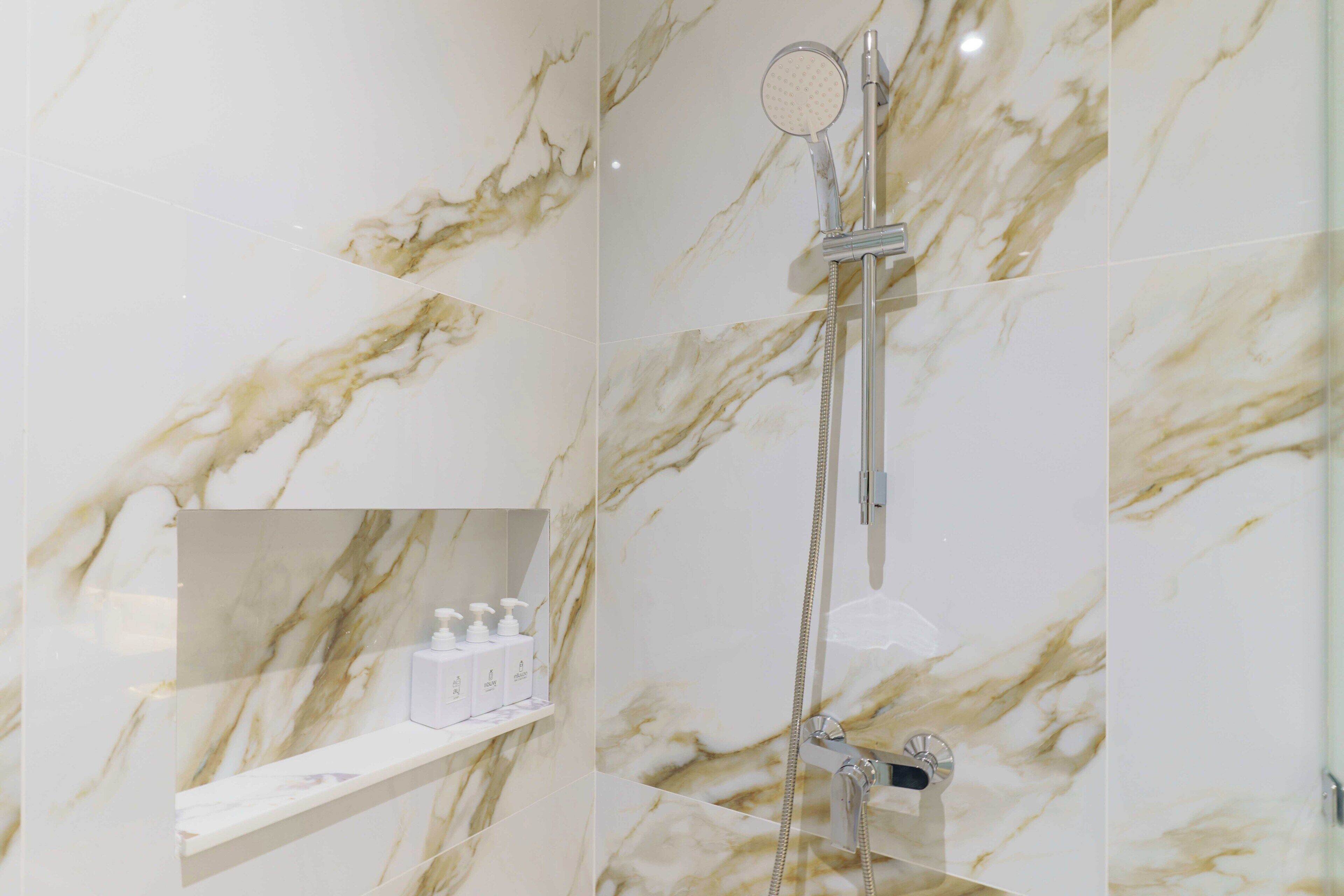 A bathroom with marble walls, a shower, and a shelf with toiletries.