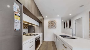 A modern kitchen with white cabinetry, a built-in stove, and a large island with a sink. - Skyline 2-Bed Apartment Near Metro North Ryde (North Ryde)