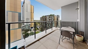 A balcony with a table and chairs, a potted plant, and a view of modern buildings. - Skyline 2-Bed Apartment Near Metro North Ryde (North Ryde)