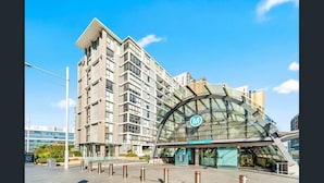 A modern hotel with a glass facade, a prominent 'M' logo, and a curved entrance. - Skyline 2-Bed Apartment Near Metro North Ryde (North Ryde)