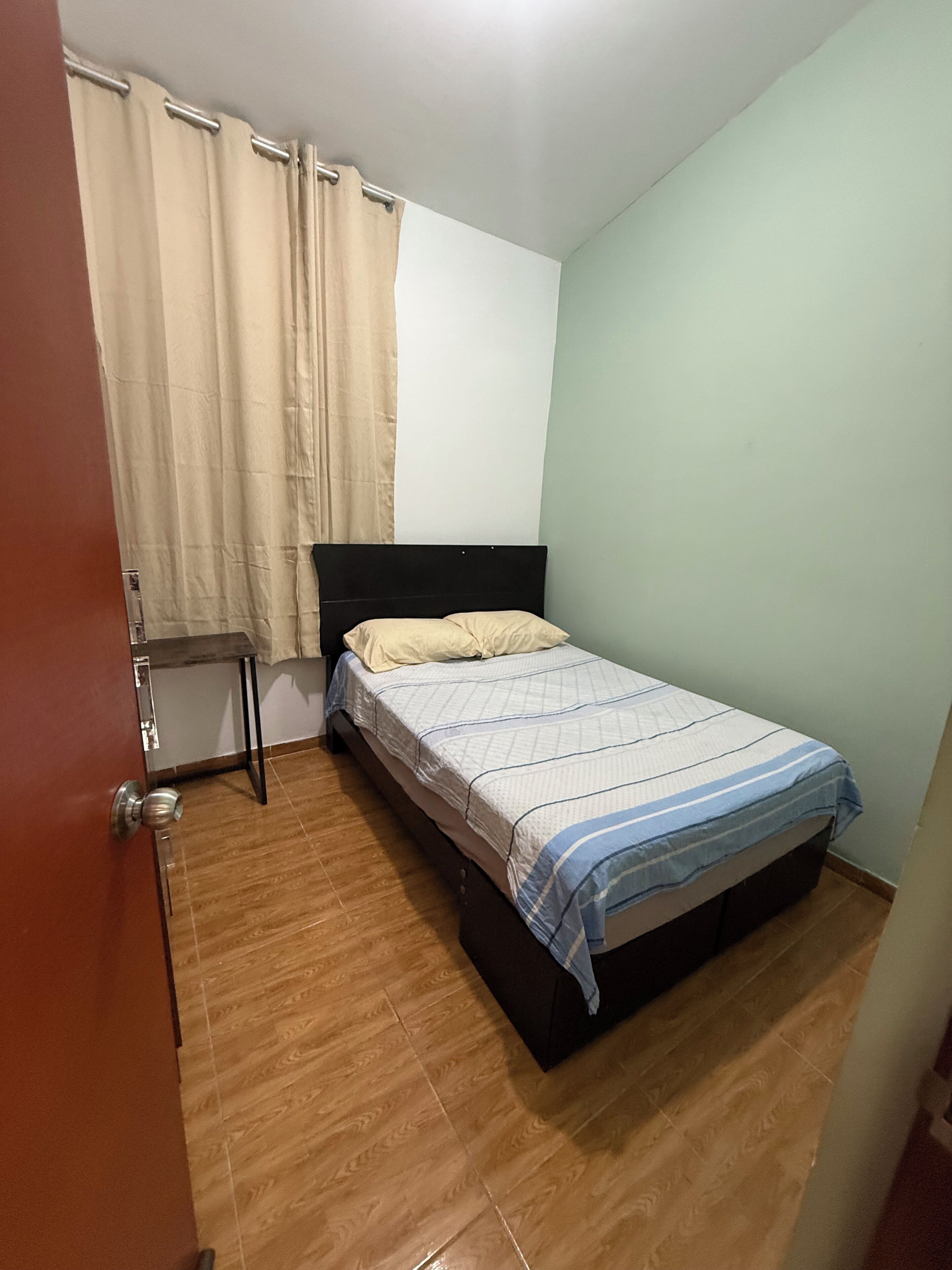 A bedroom with a bed, a door, and a curtain.
