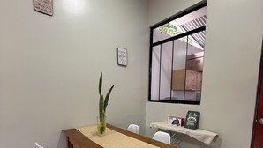 A dining area with a wooden table, white chairs, a potted plant, and a window with a view. - Relax Garden House (Moyobamba)