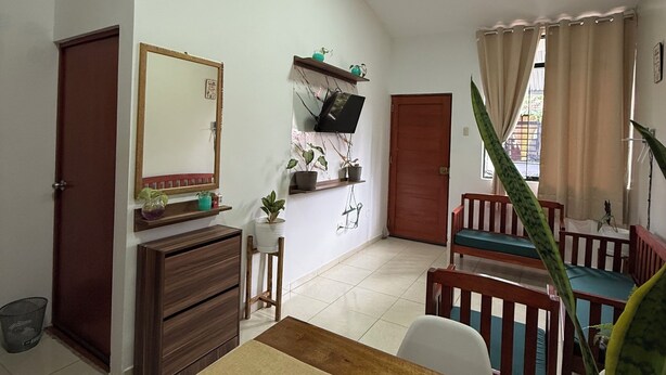 A room with a wooden dresser, a mirror, a shelf with plants, a window with curtains, and a wooden bench. - Relax Garden House (Moyobamba)