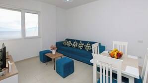 A modern living room with a blue sofa, a small table with a vase, and a dining area with a fruit bowl. - Richard Sea View Apartment (Qendër Vlorë)