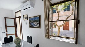 Un salón de conferencias con una mesa de vidrio, sillas, un florero, un aire acondicionado, obras de arte enmarcadas y una ventana con vistas a un árbol y un edificio.