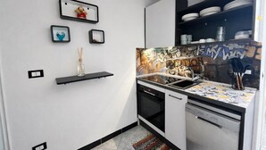 Cocina compacta con lavavajillas, horno y salpicadero con arte callejero. Hay estantes en la pared con platos y una pequeña fotografía enmarco.