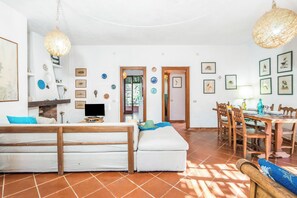 A room with a sofa, dining table, chairs, and a TV.