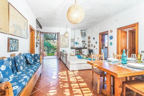 Ampla sala de estar com sofá, mesa de jantar e cozinha ao fundo.