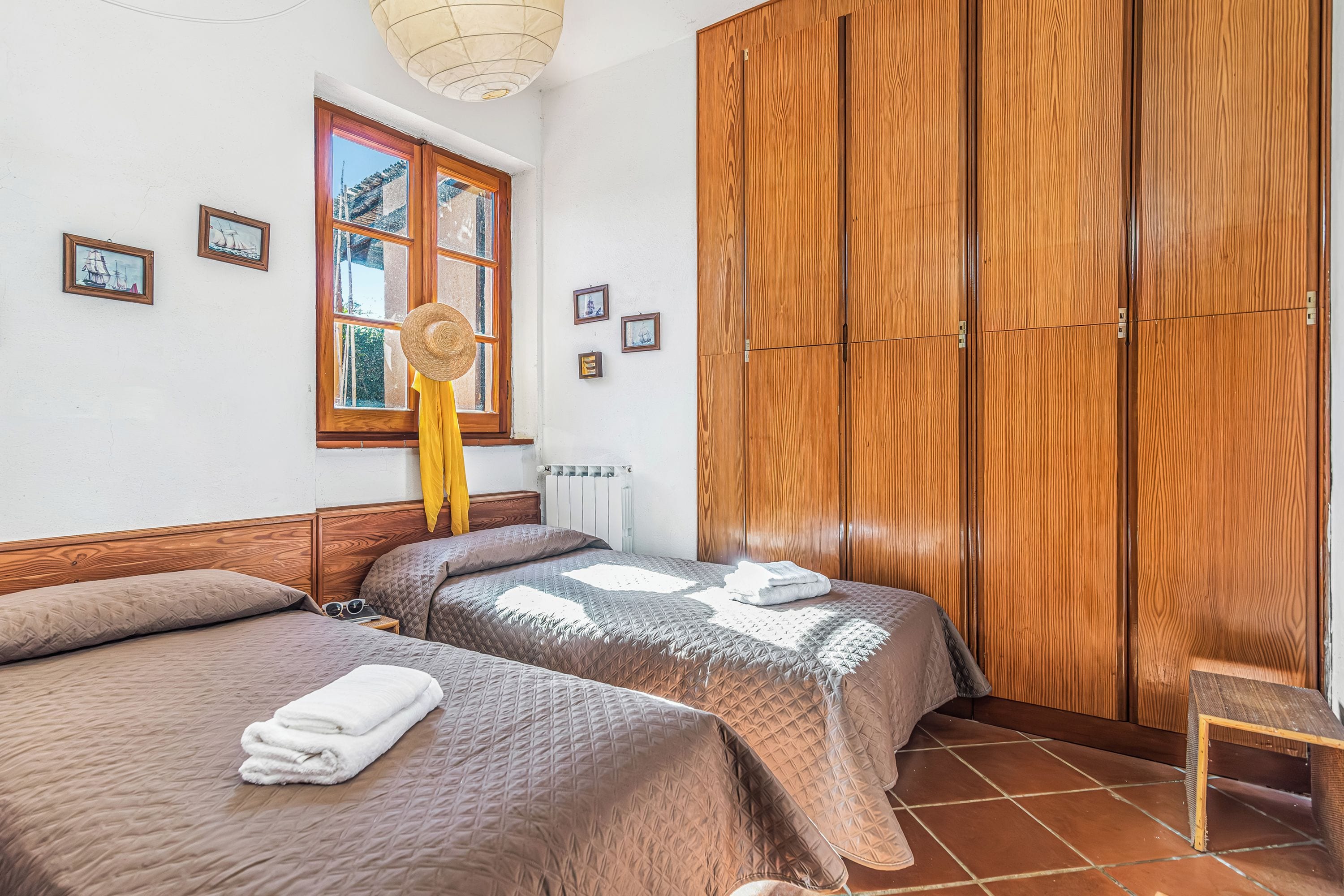 Habitación con dos camas, armario de madera, ventana con cortinas e imágenes colgadas en la pared.
