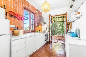 Una cocina con protector contra salpicaduras de ladrillo, muebles blancos, estufa y una lámpara colgante.