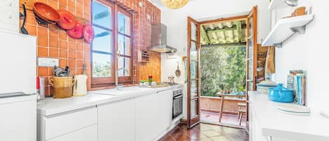 A kitchen with a brick backsplash, white cabinetry, a stove, and a hanging light fixture.