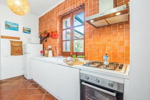 Eine Küche mit Gasherd, Backofen, weißen Schränken, einem Fenster mit Ausblick und einer abgehängten Kochutensilienstange.