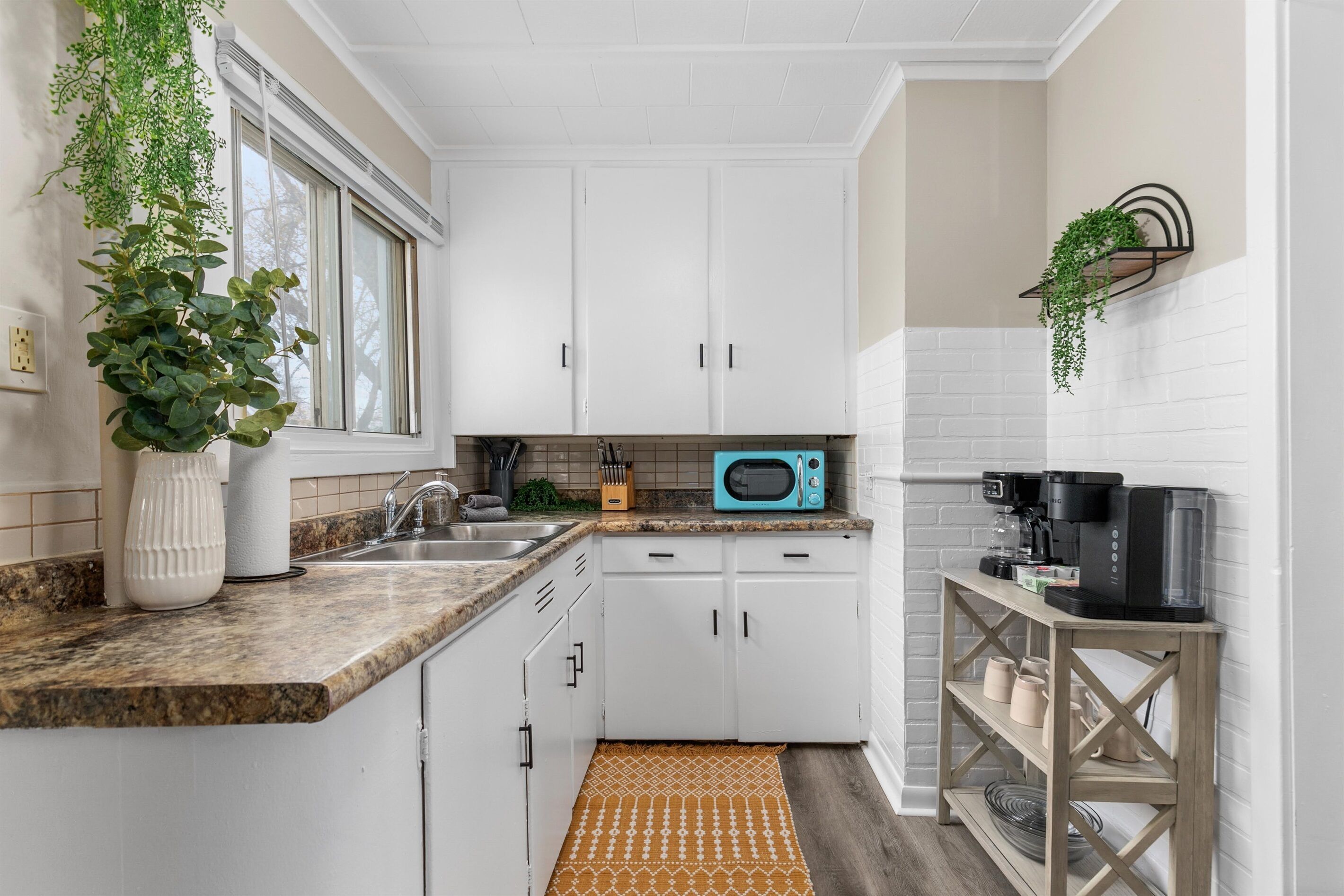 A kitchen with white cabinets, a microwave, a coffee maker, and a hanging plant.