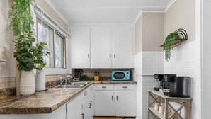 Uma cozinha com armários brancos, micro-ondas, cafeteira e planta pendente.