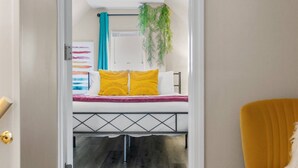 Corredor que dá para um quarto com uma cama, uma cadeira amarela e uma luminária no teto.