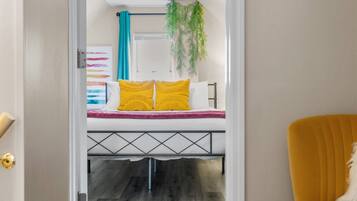 A hallway leading to a bedroom with a bed, a yellow chair, and a ceiling light.