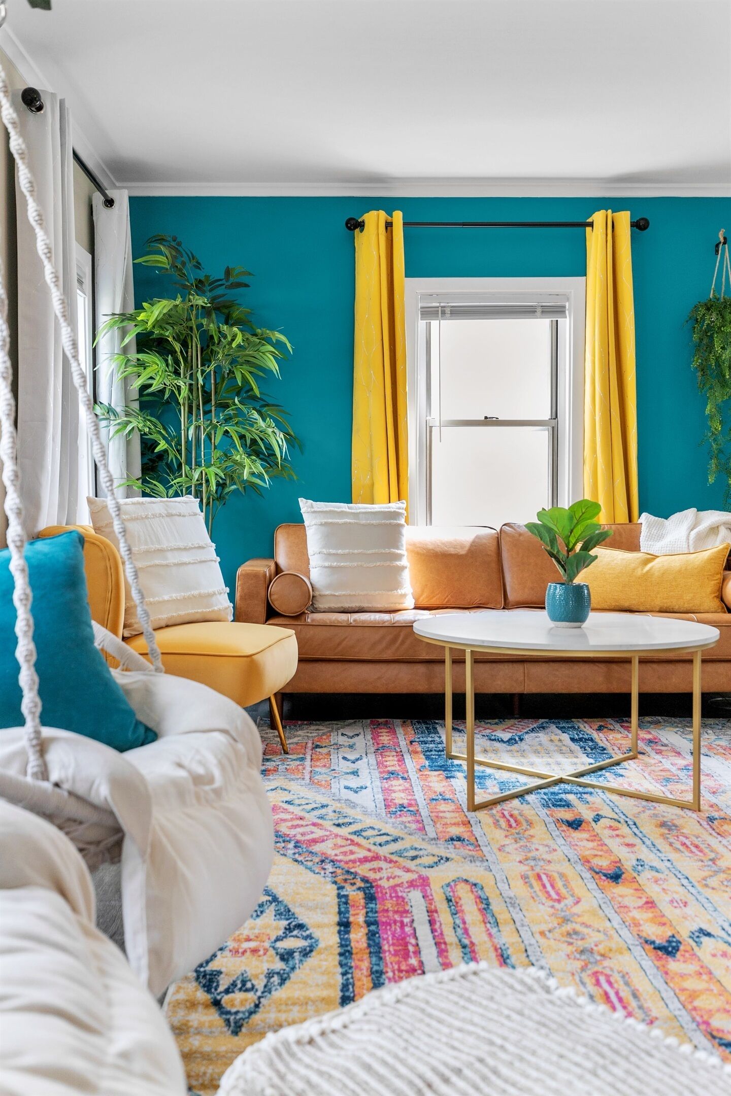 Una habitación con un sofá, una mesita, una planta colgante y una ventana con cortinas.