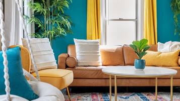 Una habitación con un sofá, una mesita, una planta colgante y una ventana con cortinas.