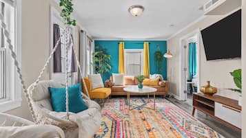 Una sala de estar con una silla colgante, un sofá, una mesa de centro y un tapiz colorido.