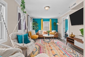 Una sala de estar con sofá, sillón colgante, mesa de centro y alfombra colorida.