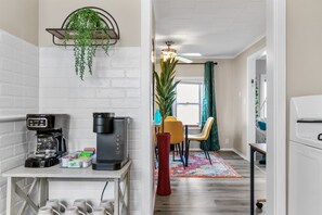 A modern kitchen with a coffee maker, a red vase, and a dining area with chairs and a table. - Cozy Oshkosh Home Minutes from UW, EAA & Downtown (Oshkosh)