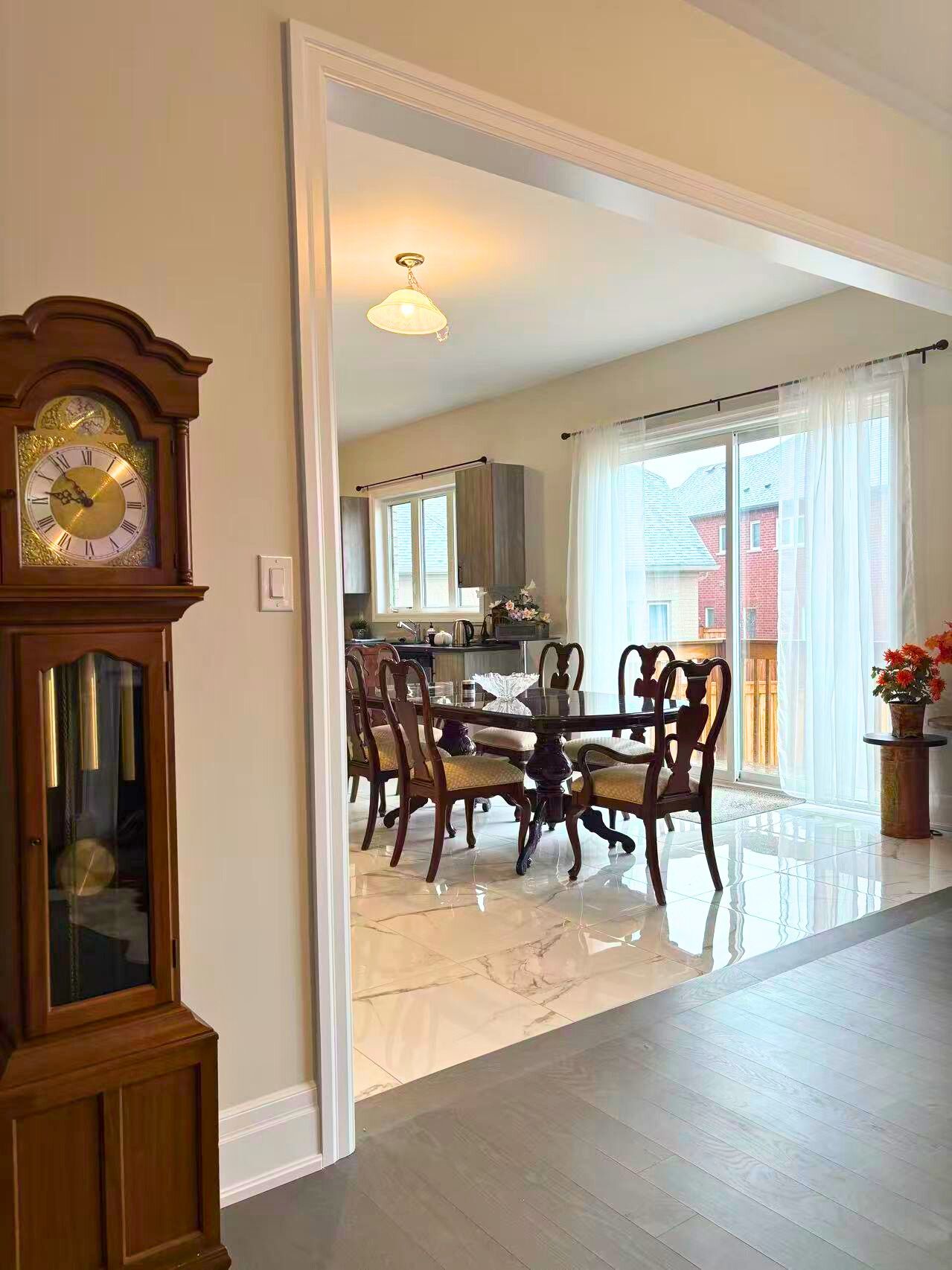 A dining area with a wooden table and chairs, a large wall clock, and a view into a kitchen.