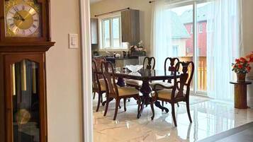 A dining area with a wooden table and chairs, a large wall clock, and a view into a kitchen.