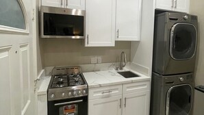 Une cuisine compacte avec des meubles blancs, une cuisinière en acier inoxydable, un four à micro-ondes, un évier et un lave-linge et un sèche-linge superposés.