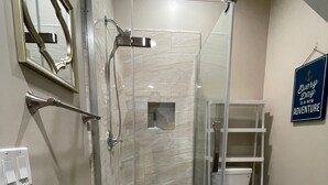 Une douche avec une porte en verre, des toilettes et une petite étagère.