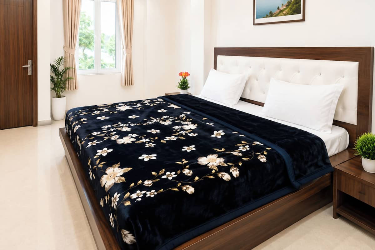 Un dormitorio con cama, mesita de noche, ventana con cortinas, planta en maceta y un cuadro en la pared.